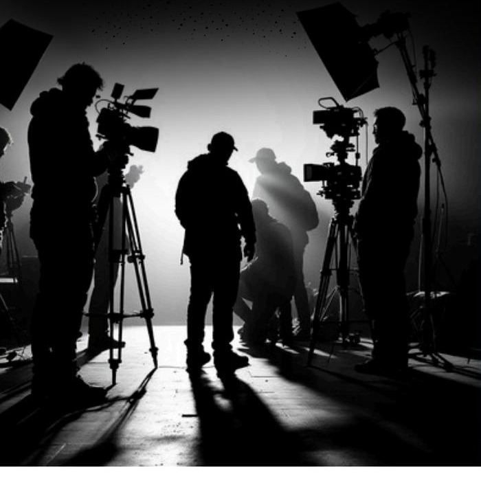 Film crew silhouetted on set, lighting rigs and cameras framing the shot