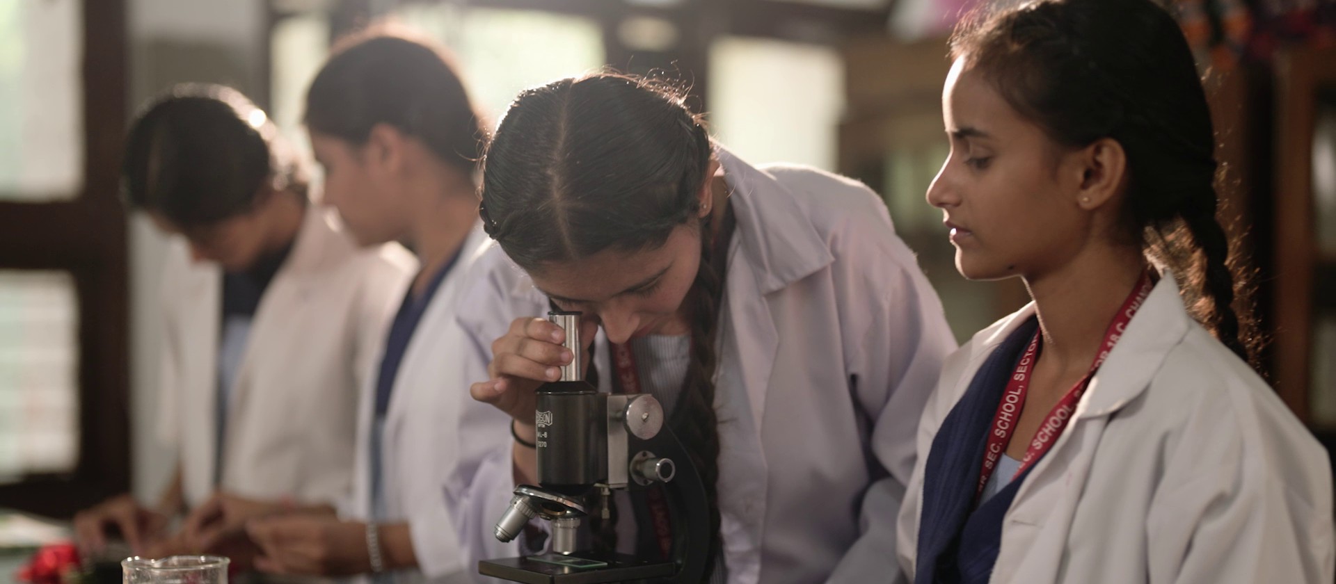 Students examining a specimen under a microscope in a school science lab